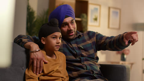 Sikh-Father-And-Young-Son-Wearing-Turbans-Sitting-On-Sofa-At-Home-Talking-Together